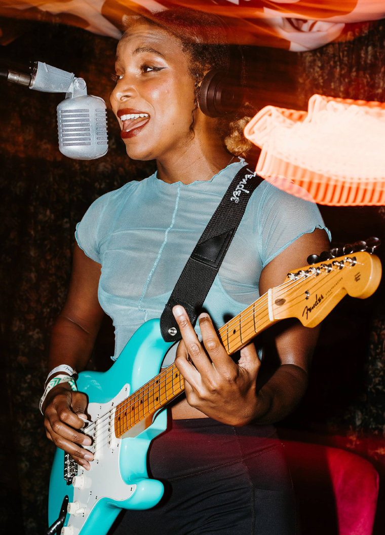 A photo of a woman singing while playing a Fender guitar at the Fender house activation.