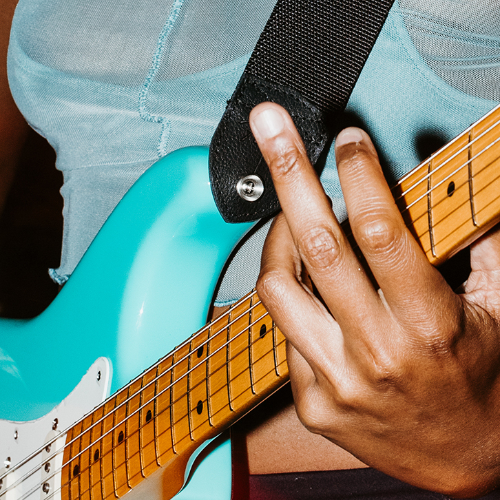 A close up from an activation McGarrah Jessee did for Fender. In the picture, we see the hand of a woman of color holding a teal Fender guitar.