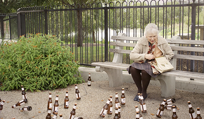 Still image from a Shiner White Wing commercial depicting a woman feeding birds, but instead of birds, it's bottles of beer.